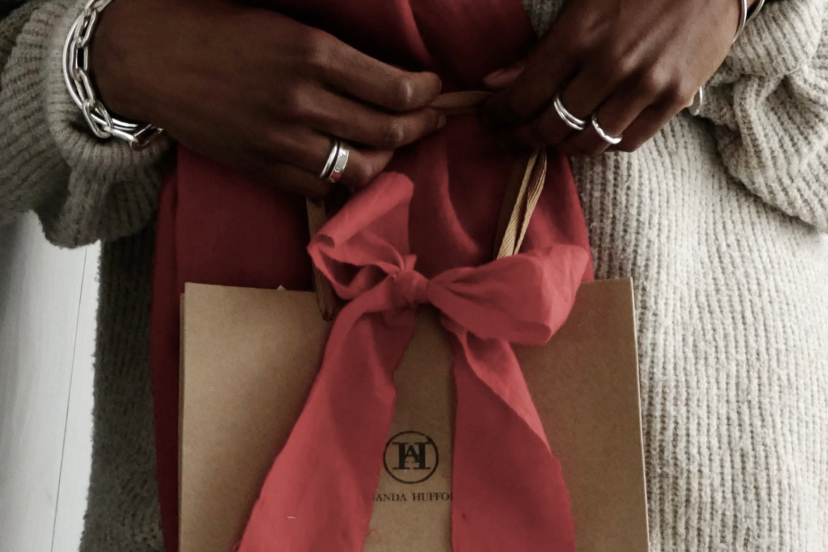 Model holding an Amanda Hufford Studio gift bag and bow, hands adorned with stacked and layered handmade Amanda Hufford Studio jewelry
