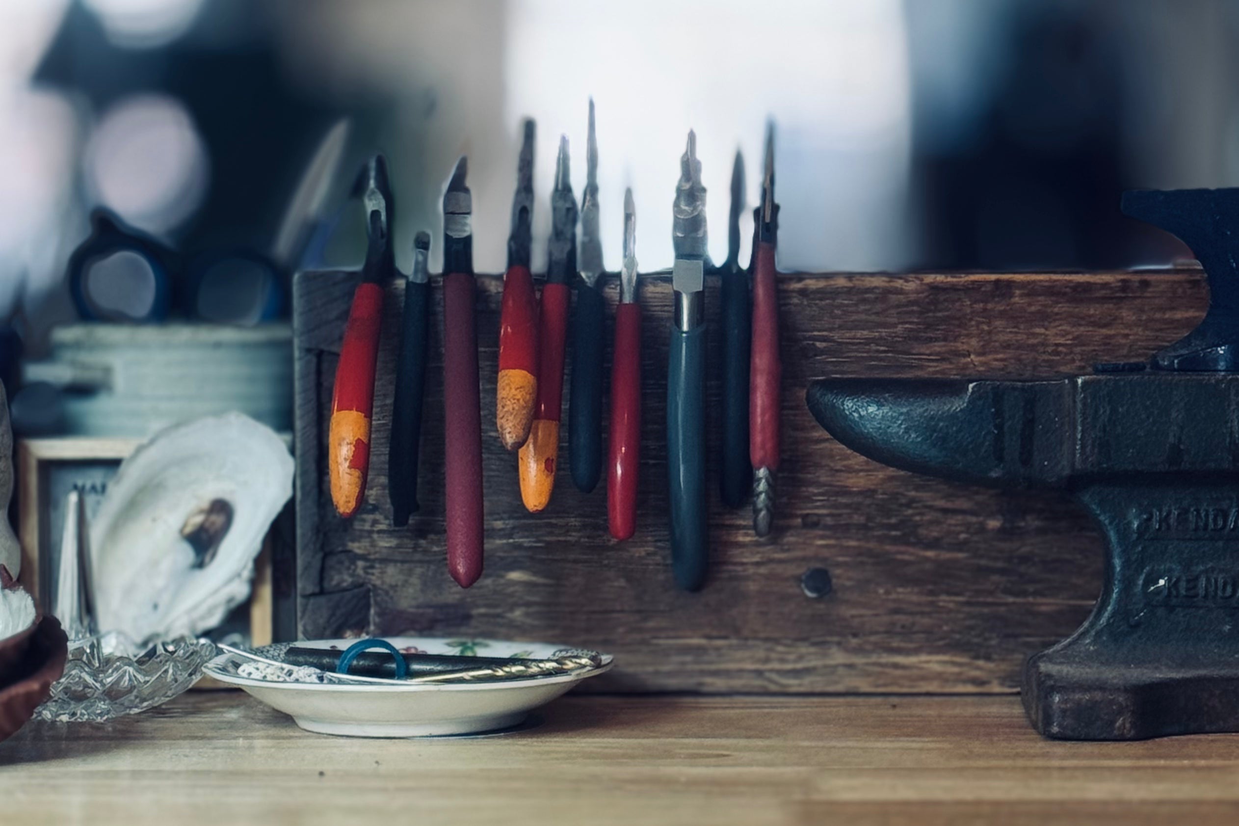Amanda Hufford's jeweler's bench with an anvil, pliers lined up in a holder, and an oyster shell among various studio tools
